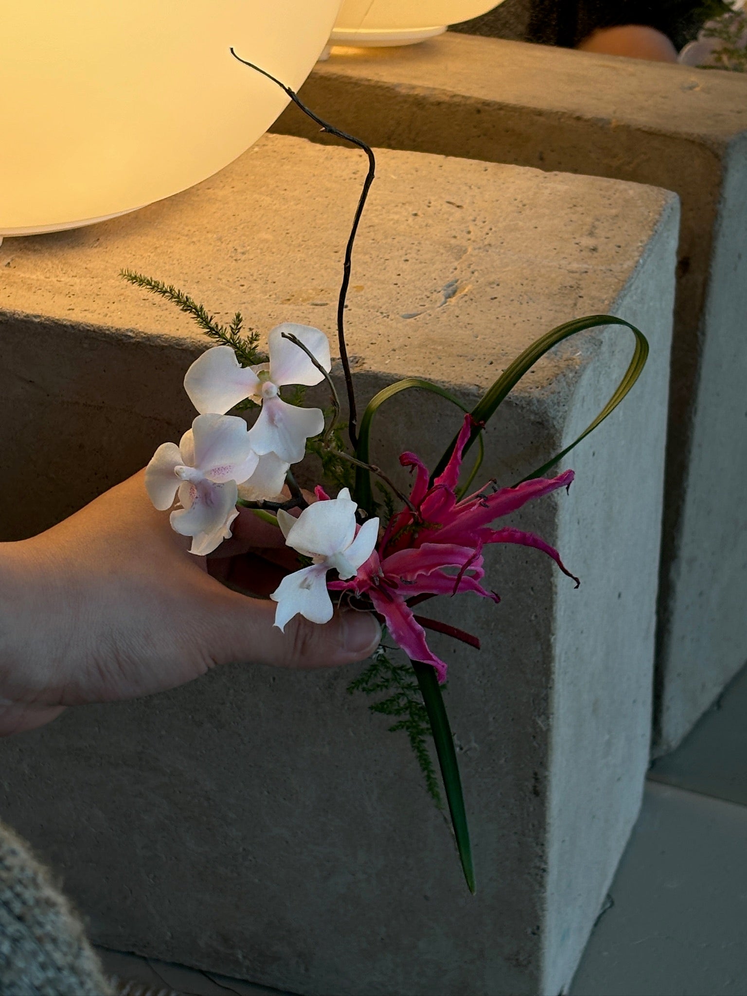 A unique boutonniere featuring delicate white orchids and vibrant pink nerine, with a modern touch of dark, curving vine tendrils.