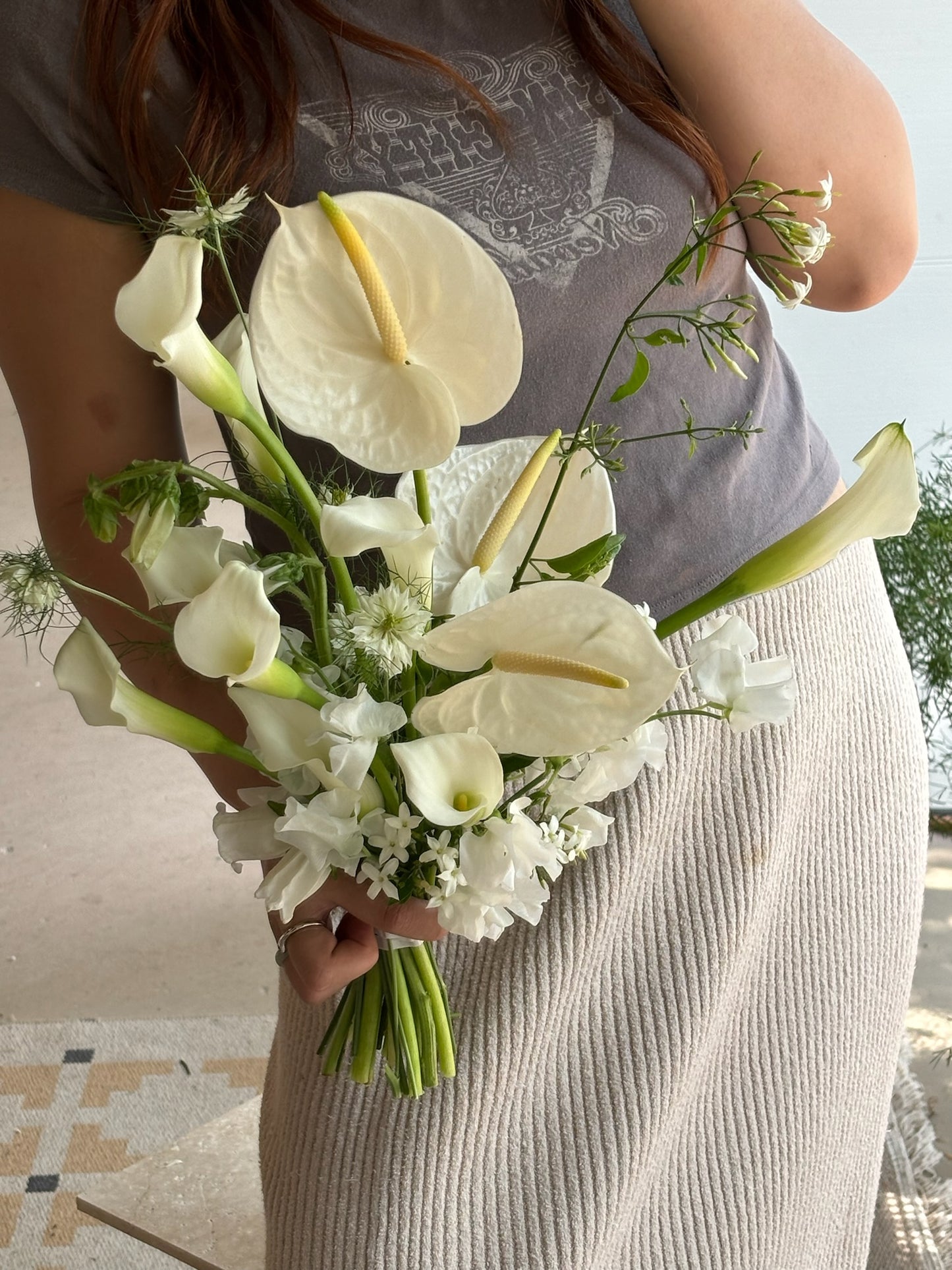 A modern bridal bouquet featuring white anthuriums, calla lilies, and delicate green foliage, designed in a soft, flowing arrangement for a minimalist yet elegant look.